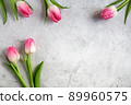 Blooming pink tulips flowers with green leaves on gray concrete background flat lay with copy space for congratulations, advertising or design. Minimalism concept. 89960575