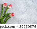 Three blooming pink tulips flowers with green leaves on gray concrete background flat lay with copy space for congratulations, advertising or design. Minimalism concept. 89960576
