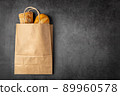 Disposable paper bag from a supermarket recyclable with whole baked loaves of bread flatlay on dark background with copy space. 89960578