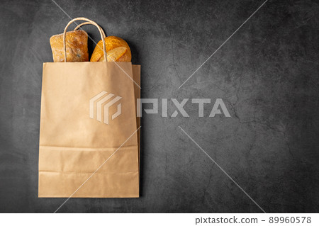 Disposable paper bag from a supermarket recyclable with whole baked loaves of bread flatlay on dark background with copy space. 89960578