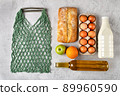 Set of grocery items with healthy food in eco string bag milk, eggs, oil, bread and fruits flat lay on gray background. Buying products for home on store. 89960590
