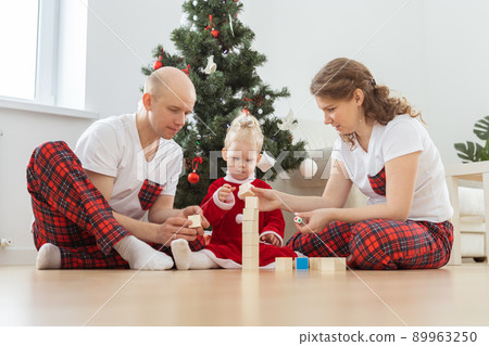 Toddler child with cochlear implant plays with parents under christmas tree - deafness and innovating medical technologies for hearing aid Toddler child with cochlear implant plays with parents under christmas tree - deafness and innovating medical technologies for hearing aid 89963250