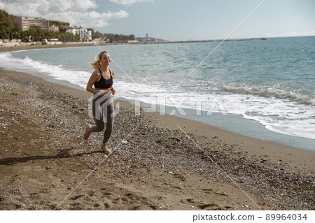 Sporty young female enjoying jogging along beautiful coast Sporty young female enjoying jogging along beautiful coast 89964034