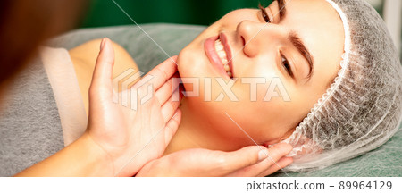 Plastic surgery and beauty concept. Professional cosmetician examining and touching the face of the beautiful young caucasian smiling woman in a clinic of esthetic cosmetology Plastic surgery and beauty concept. Professional cosmetician examining and touching the face of the beautiful young caucasian smiling woman in a clinic of esthetic cosmetology 89964129