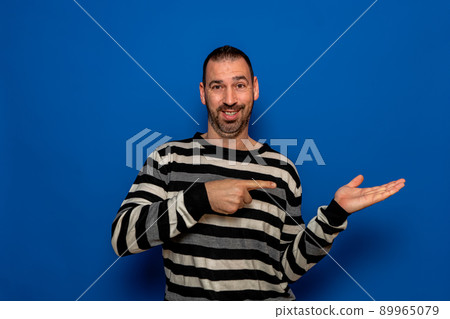 Surprised man in striped sweater pointing left with his finger, shouting WOW, isolated on blue background with copy space for your text. shock content. Surprised man in striped sweater pointing left with his finger, shouting WOW, isolated on blue background with copy space for your text. shock content. 89965079