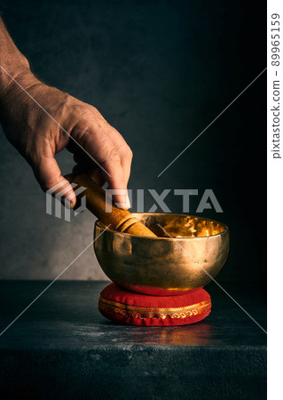 a hand with a hammer and a Tibetan bowl on a dark background 89965159