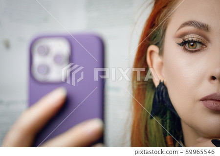 Red-haired girl takes selfie on front camera of smartphone. Female blogger runs a blog about fashion and makeup. Woman with Gothic-style jewelry with proud expression on her face. Witch aesthetic. 89965546