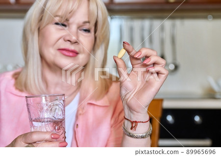 Mature woman holding vitamin pill supplement in her hand and a glass of water Mature woman holding vitamin pill supplement in her hand and a glass of water 89965696