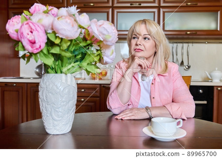 Beautiful mature woman sitting at home with bouquet of flowers Beautiful mature woman sitting at home with bouquet of flowers 89965700