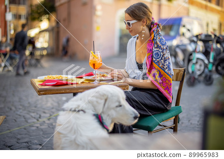 Woman eating italian pasta while sitting with a dog at restaurant on the street in Rome 89965983