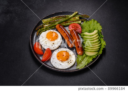 A delicious nourishing breakfast with fried eggs, sausages, asparagus, tomatoes, avocado, spices and herbs 89966184