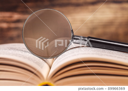 the magnifying glass is lying on an open book. space for text the magnifying glass is lying on an open book. space for text 89966369