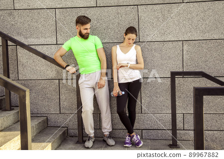 Young sporty couple are resting and check their fitness watch together, drinking water. sport and technology concepts. Young sporty couple are resting and check their fitness watch together, drinking water. sport and technology concepts. 89967882