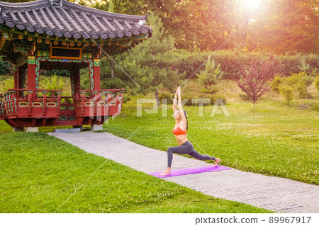 Cheerful young beautiful woman practicing and posing yoga in the east Asian park. warrior pose. 89967917