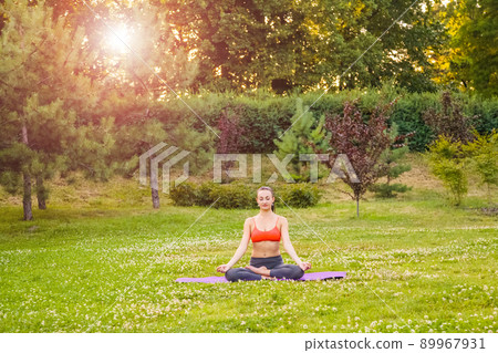 Cheerful young beautiful woman practicing and posing yoga in the park. 89967931