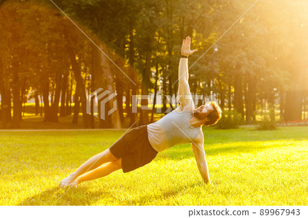 Strong young adult man doing yoga. Stay in plank on one arm. Looking up to the sky. Outdoor shot Strong young adult man doing yoga. Stay in plank on one arm. Looking up to the sky. Outdoor shot 89967943