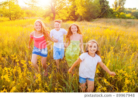 four happy beautiful children running playing moving together in the beautiful summer day. jumping and looking at camera with happiness and toothy smile. 89967948
