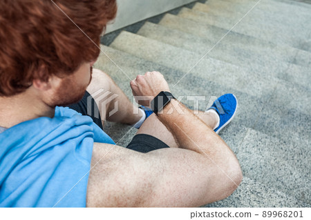 View from above. Athlete looking at smart watch and considers calories after hard training. Outdoor shot. Summertime View from above. Athlete looking at smart watch and considers calories after hard training. Outdoor shot. Summertime 89968201