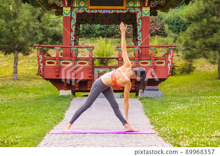 Cheerful young beautiful woman practicing and posing yoga in the east Asian park. Cheerful young beautiful woman practicing and posing yoga in the east Asian park. 89968357
