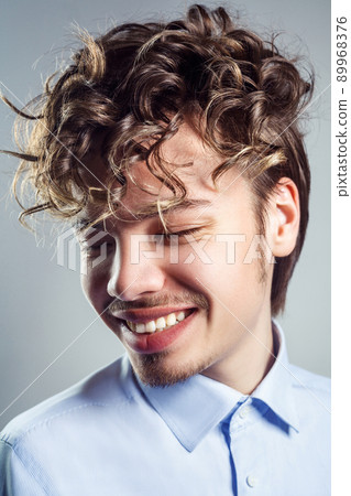 Portrait of young man with curly hairstyle. studio shot. toothy smile and closed eyes. Portrait of young man with curly hairstyle. studio shot. toothy smile and closed eyes. 89968376