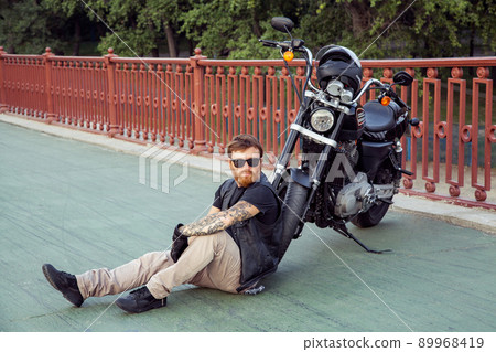 bearded motorcyclist man with his motorbike on summertime posing. 89968419
