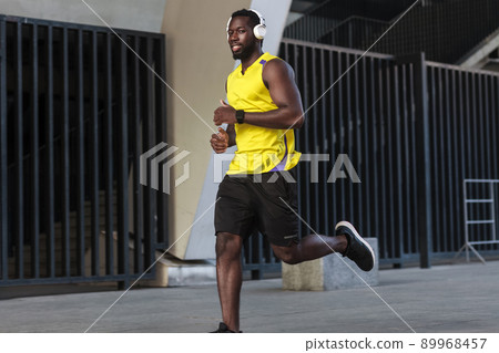 Close up portrait of toothy smiling african runner training and jogging on a summer day outdoors wearing yellow color sportswear Close up portrait of toothy smiling african runner training and jogging on a summer day outdoors wearing yellow color sportswear 89968457