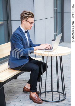Attractive young freelancer with blue casual suit with laptop and coffee sitting and working. looking at display and smilling. Attractive young freelancer with blue casual suit with laptop and coffee sitting and working. looking at display and smilling. 89968462