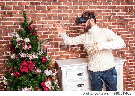 loneliness and illusion of new year. the portrait of bearded man with virtual reality glasses near new year's tree. 89968463