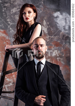 Portrait of businessman standing near stepladder and looking at camera with ginger woman standing on old stepladder. Studio shot. Portrait of businessman standing near stepladder and looking at camera with ginger woman standing on old stepladder. Studio shot. 89968482