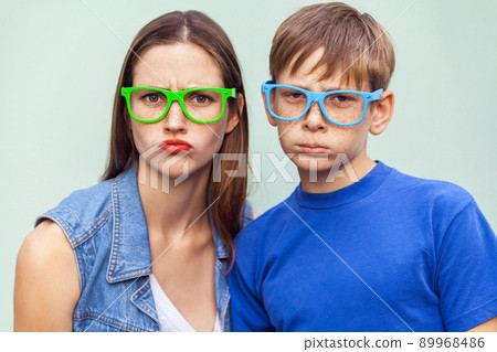 Family, bad emotions and feelings. Older sister and her brother with freckles, posing over light blue background together, looking at camera with unhappy faces. Studio shot 89968486