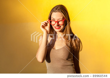 Sunglasses. Playfully girl wink at camera, and toothy smile. Isolated on yellow background, studio shot 89968544