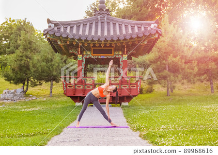 Cheerful young beautiful woman practicing and posing yoga in the east Asian park. triangle pose. Cheerful young beautiful woman practicing and posing yoga in the east Asian park. triangle pose. 89968616
