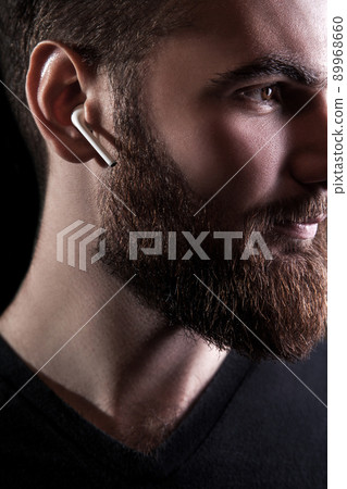 Young bearded man with wireless earphones on his ears. studio shot on black background. Young bearded man with wireless earphones on his ears. studio shot on black background. 89968660