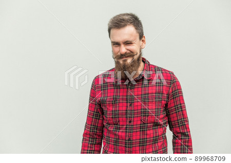 Flirt and wink. Carefree bearded man winked at camera and smiling. Studio shot, gray background 89968709