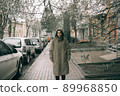 Traveling young woman in green raincoat with hood walking down street 89968850