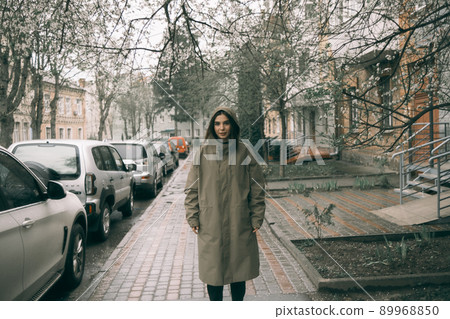 Traveling young woman in green raincoat with hood walking down street 89968850