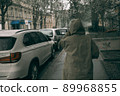 Traveling young woman in green raincoat with hood walking down street 89968855