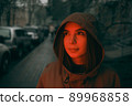 Young happy woman wearing raincoat is feeling free and smiling under the rain. red light 89968858