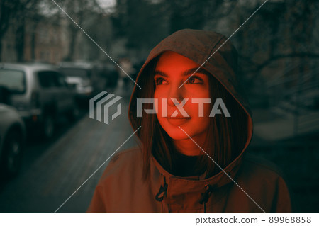 Young happy woman wearing raincoat is feeling free and smiling under the rain. red light 89968858