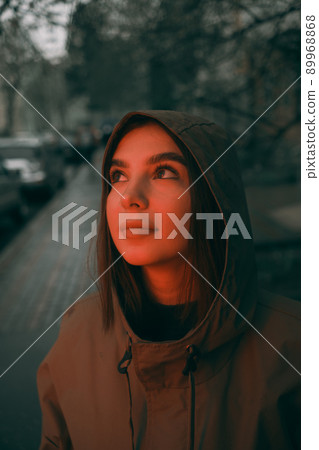 Young happy woman wearing raincoat is feeling free and smiling under the rain. red light 89968868