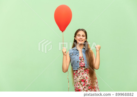 Its winn! The beautiful blonde teenager with red balloons on a green background. Isolated studio shot 89968882