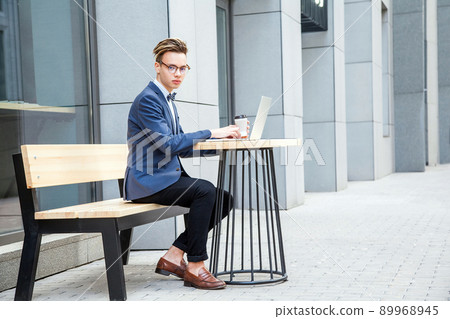 Attractive young freelancer with blue casual suit with laptop and coffee sitting and working. looking at camera and smilling. Attractive young freelancer with blue casual suit with laptop and coffee sitting and working. looking at camera and smilling. 89968945