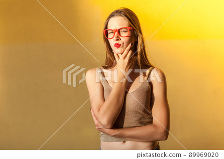 Hmm. Think about that. Young adult beautiful freckled woman, touching her chin, thinking, and looking seriously at camera. isolated on yellow background, studio shot 89969020
