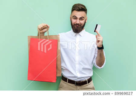 Young adult businessman using credit card for online shopping or banking. Holding credit card on hands and looking at camera and smile. Indoor, studio shot. Light green background 89969027