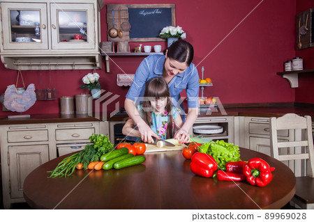 Happy mother and daughter enjoy making and having healthy meal together at their kitchen. they are making vegetable salad and having fun together. mom take care of her daughter and tech how to cook. 89969028