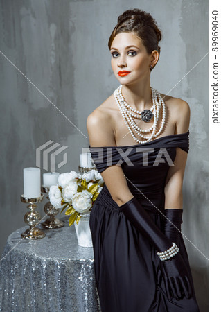 Beautiful young fashion caucasian model in black long dress and fashion makeup and beautiful hairdo posing sitting on the chair and looking at camera. Studio shot. Beautiful young fashion caucasian model in black long dress and fashion makeup and beautiful hairdo posing sitting on the chair and looking at camera. Studio shot. 89969040