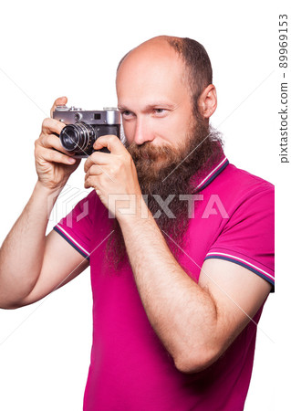 The portrait of bald bearded man photographer with pink t shirt holding classic camera. isolated on white background. studio shot. The portrait of bald bearded man photographer with pink t shirt holding classic camera. isolated on white background. studio shot. 89969153