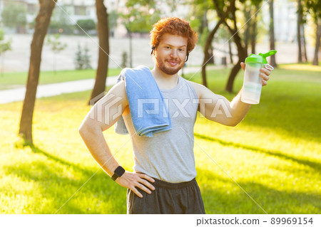 Funny redhead muscular man showing bottle and lookingat camera. Outdoor shot Funny redhead muscular man showing bottle and lookingat camera. Outdoor shot 89969154