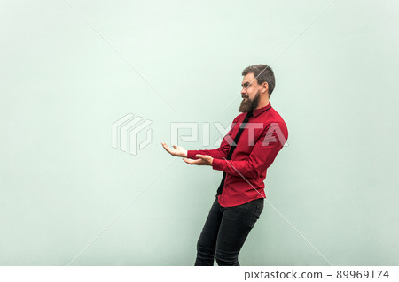 Bearded man in casual clothes, keeps something heavy. Studio shot, gray background 89969174
