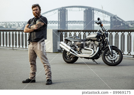 bearded motorcyclist man with his motorbike on summertime posing. 89969175